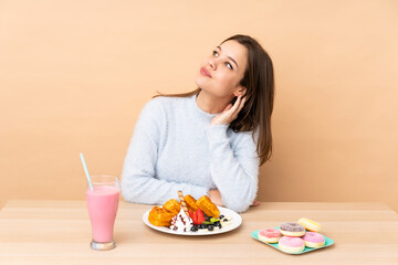 Obraz na płótnie Canvas Teenager girl eating waffles isolated on beige background thinking an idea