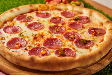 Traditional italian Pizza Pepperoni with salami, mozzarella and basil on green grass background