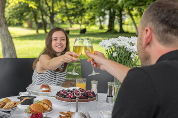 Brunch Choice Dining Food Options Eating Concept. Couple having a brunch with sparkling wine outdoors. Glasses of sparkling wine in hands, cheers! Benedict egg and other food on table.
