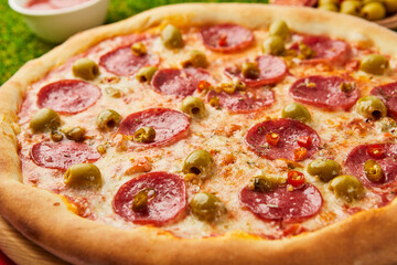 Traditional italian Pizza Pepperoni with salami, mozzarella, olives and basil on green grass background