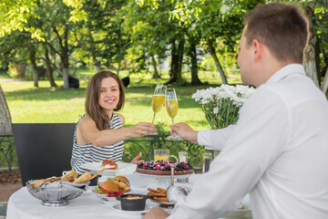 Brunch Choice Dining Food Options Eating Concept. Couple having a brunch with sparkling wine outdoors. Glasses of sparkling wine in hands, cheers! Benedict egg and other food on table.