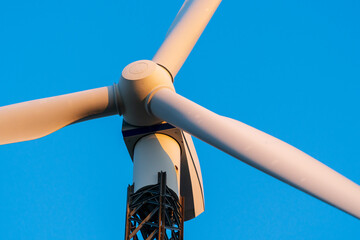 Wind turbine against a clear blue sky at a wind turbine farm at sunset. Low angle view, close-up on propeller. Theme of renewable energy, clean power generation and sustainable energy concepts. © fotorauschen