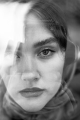 Close-up portrait of beautiful girl through reflections in window, black and white photo