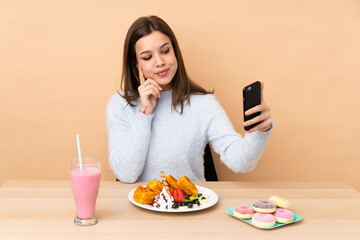 Teenager girl eating waffles isolated on beige background making a selfie