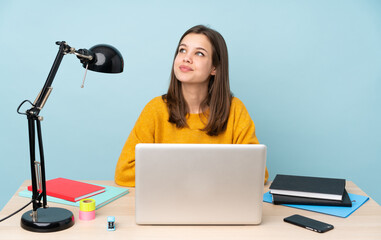 Student girl studying in her house isolated on blue background looking up while smiling