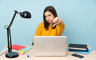 Student girl studying in her house isolated on blue background showing thumb down with negative expression