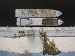 A crane near a cargo ship in a frozen bay. Aerial drone view. Winter snowy morning.