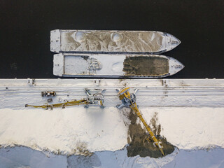 A crane near a cargo ship in a frozen bay. Aerial drone view. Winter snowy morning.