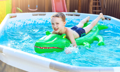 Boy on inflatable crocodile float in outdoor swimming pool at home. Swim aids and wear for children