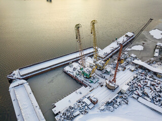 A crane near a cargo ship in a frozen bay. Aerial drone view. Winter snowy morning.