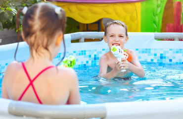 Happy laughing child playing with water gun in outdoor swimming pool on summer day. Kids play and learn to swim. Pool toys and water fun for family with children