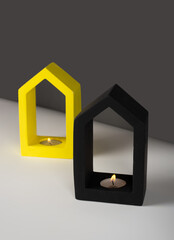Creative diagonal isometric projection composition. Still life. Shadows on the gray wall. house-shaped concrete candlestick black and yellow color with soy wax burning scented candle. Minimalistic