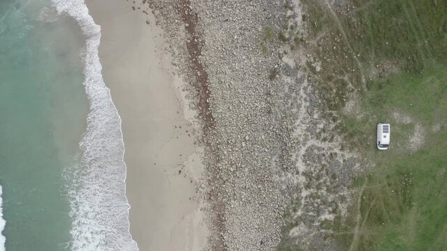 Wild beach green landscape drone top aerial view with waves crashing and a camper van, in North of Spain