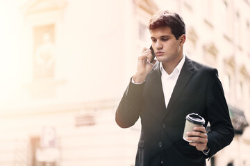 a serious man standing in the street in a suit is talking on the phone in the open air. businessman getting bad news on the street. Holds a cup of drink.