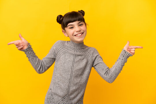 Little caucasian girl isolated on yellow background pointing finger to the laterals and happy