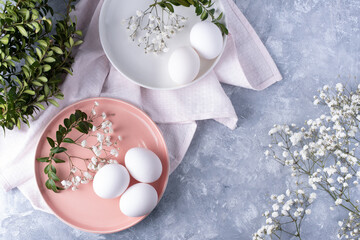 White eggs on plates on a gray background with green branches and gisophila on a gray background.