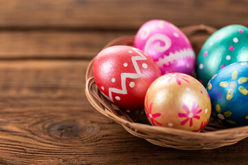 Fototapeta na wymiar Five easter eggs trendy colored deep blue, green, orange, magenta and golden decorated in basket on old wooden table. Copy space for text.