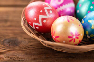 Five easter eggs trendy colored deep blue, green, orange, magenta and golden decorated in basket on old wooden table. Copy space for text.