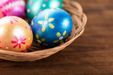 Obraz na płótnie Canvas Five easter eggs trendy colored deep blue, green, orange, magenta and golden decorated in basket on old wooden table. Copy space for text.