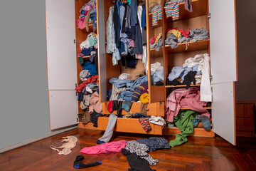 Wardrobe clutter. A wardrobe full of used clothes. Scattered clothes on the floor