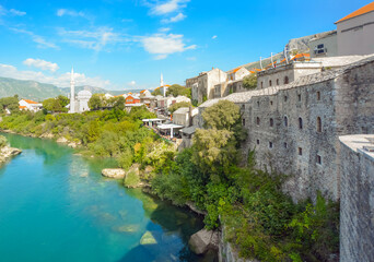 Fototapeta na wymiar The river Neretva flows by the ancient wall surrounding the old town and village of Mostar, Bosnia and Herzegovina.