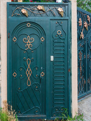 Dark turquoise iron gate with a forged pattern in the form of a golden vine, monograms and gilded...