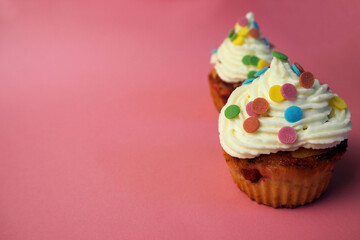 two diet yogurt muffins with red currant smeared with white cream and mascarpone decorated with colorful round splashes on a pink background side view . homemade cakes