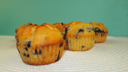 Several blueberry muffins, pea flour, rice flour, eggs, and yogurt stand on a white surface with a view of a turquoise wall side view . homemade cakes