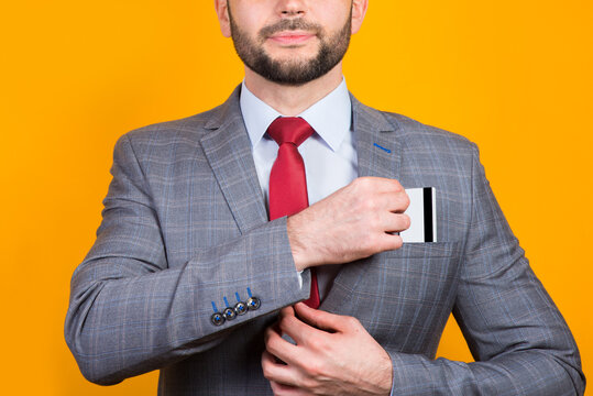 A man in a business suit puts a bank card in a kaman close-up on a yellow background
