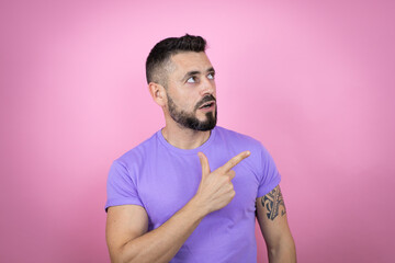 Young handsome man wearing casual t-shirt over pink background smiling and pointing with hand and finger to the side