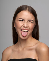 Young beautiful female model close-up studio beauty portrait. Girl with natural make-up and long brunette straight hair. Happy crazy woman shoing her tongue and winking