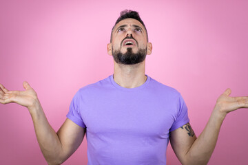 Young handsome man wearing casual t-shirt over pink background clueless and confused expression...