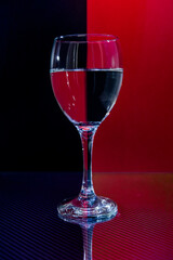 Small glassy goblet with water standing on glassy carbon reflecting surface with reflecting red and black background