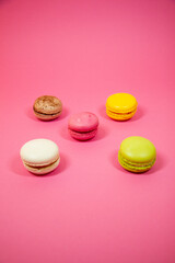 Sweet and colourful french macaroons in row on the pink background. Sweet dessert. Yellow, pink, white, brown and green macaroons.