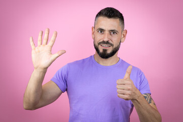 Young handsome man wearing casual t-shirt over pink background showing and pointing up with fingers number six while smiling confident and happy