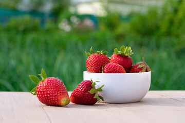 Red ripe strawberries in white bowl on blurred green background.Summer berries garden harvest
