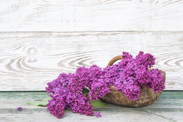 Obraz na płótnie Canvas Happy Mothers's day greeting card. Bunch of purple lilacs in vintage wicker basket on rustic wooden background. Space for text