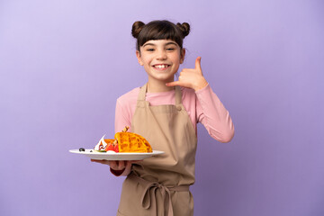 Little caucasian girl holding waffles isolated on purple background making phone gesture. Call me back sign