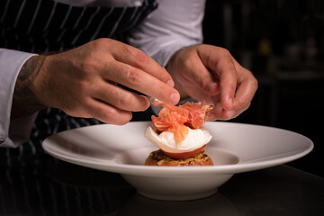Chef cook preparing eggs in his kitchen. Eggs Benedict on toasted muffins with ham and sauce. Breakfast Buffet Concept, Breakfast Time. Various brunch on the table. 