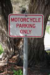 Fototapeta premium Sign in front of a tree at a parking lot marking a space for MOTORCYCLES PARKING ONLY