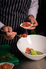 Chef cook preparing salad with salmon and avocado in his kitchen. Freezer food prepare in process vegetarian salad by chef hand in home kitchen. Dark black background with Text area for design menu 
