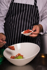 Chef cook preparing salad with salmon and avocado in his kitchen. Freezer food prepare in process vegetarian salad by chef hand in home kitchen. Dark black background with Text area for design menu 