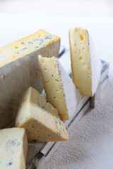 Soft white cheese with blue mold in a white wooden box on a black background. Vertical photo. Several pieces of cheese.
