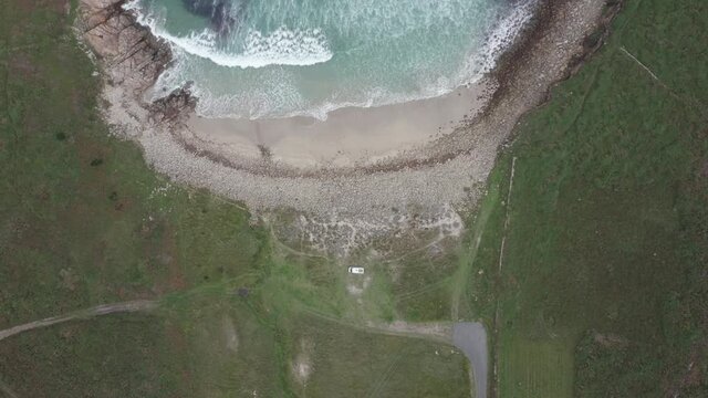 Wild beach green landscape drone top aerial view with waves crashing and a camper van, in North of Spain