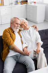 Smiling elderly woman holding hand of husband on sofa