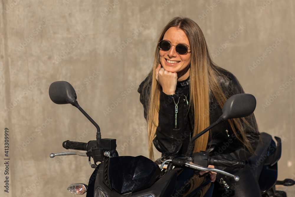 Wall mural Pretty Caucasian lady wearing a leather jacket with an all-black outfit on her motorbike