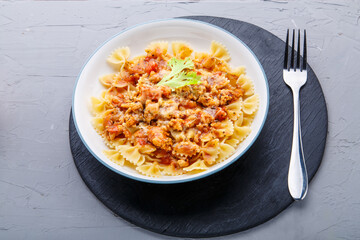 Pasta in tomato bolognese sauce on a black stand on a concrete background next to a fork