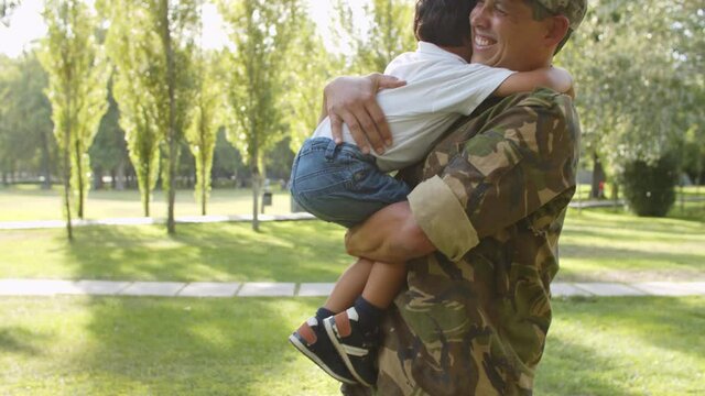Excited boy running to soldier dads open arms, daddy catching, hugging and cuddling little son. Family reunion or fatherhood concept