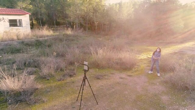Adolescente bailando delante de m&oacute;vil con mascarilla coronavirus en toma con dron al atardecer