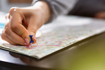 Female hand holding pushpin showing the location of a destination point on a map. Travel...